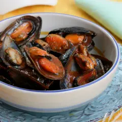 Un invitante sautè di cozze, succulente e profumate, servite in una ciotola bianca con bordo blu.