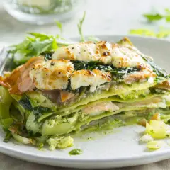 Une part de lasagne saumon épinard, gratinée au fromage, servie avec une salade verte.