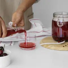 Ręce nalewają wiśniowy napój z butelki do szklanki. Może to być domowe wino, ale obawiam się, że jest za dużo cukru w winie.