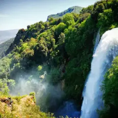 Cascata imponente nella rigogliosa montagna umbria, con valli verdi e cielo azzurro.