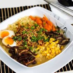 Miseczka tantanmen z makaronem, jajkiem na pół, kukurydzą, marchewką i grzybami.