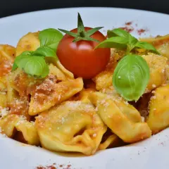 Pyszne tortellini na talerzu, polane sosem pomidorowym, ozdobione listkami bazylii i pomidorkiem.