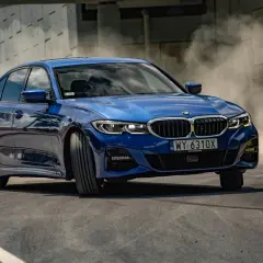 Niebieskie BMW 330i G20 w zakręcie, unosząc tumany kurzu.