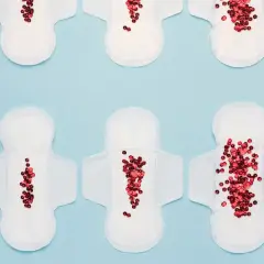 Toallas sanitarias con lentejuelas rojas que simulan el flujo menstrual, representando la dismenorrea que es.