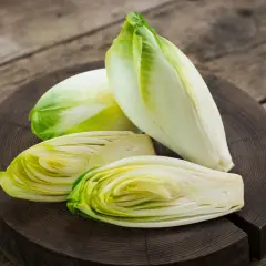 Frische Chicorée-Köpfe, einer davon halbiert, liegen auf einem Holzbrett. Perfekt für einen knackigen Chicorée-Salat.
