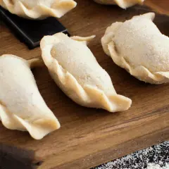 Surowe pierogi na desce. Zastanawiasz się, ile gotować pierogi, by były idealne?