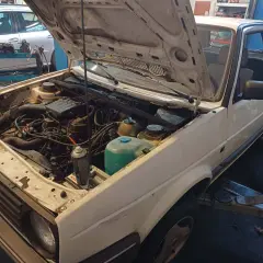 Biały Volkswagen Golf z otwartą maską, silnik gotowy do wyjęcia. Zastanawiasz się, ile kosztuje wyciągnięcie silnika?