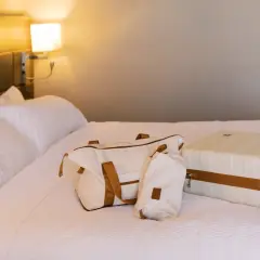 Biała walizka i torba podróżna na łóżku w hotelu.
