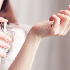 Kobieta rozpyla perfumy na nadgarstek. Zapach przypomina Niveę, otulając skórę delikatną mgiełką.