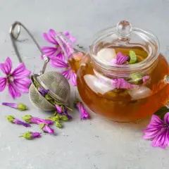 Tè alla malva in teiera di vetro, con fiori e infusore. Attenzione ai malva effetti collaterali.