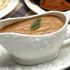Saucière en porcelaine ornée de grappes de raisin, remplie d'une onctueuse sauce foie gras, garnie d'une feuille de sauge.