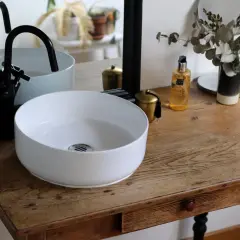 Un plan pour créer son meuble de salle de bain : vasque blanche, robinetterie noire, miroir et accessoires déco sur un meuble ancien.