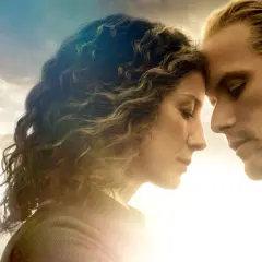Claire i Jamie, bohaterowie serialu Outlander, z czołami dotykającymi się na tle nieba.
