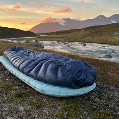 Sovsäck och liggunderlag redo för en natt i fjällen. Test av liggunderlag vid en forsande älv i solnedgången.