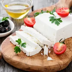 Una porzione feta fresca, tagliata a fette, con pomodorini e olive nere su un tagliere di legno.