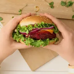 Ręce trzymają wegetariańskiego burgera z buraka, sałatą, cebulą i serem. Pyszna krowarzywa na desce.