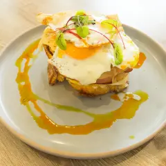 Un délicieux croque madame avec un œuf au plat coulant, du jambon et du fromage fondu, garni de jeunes pousses et servi sur une assiette avec un filet de sauce.