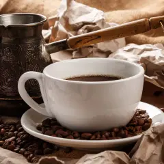 Ein traditioneller Mokkakanne und eine Tasse mit griechischem Mokka, umgeben von Kaffeebohnen und zerknülltem Papier.