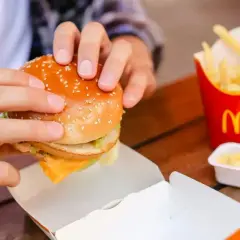Ręce trzymają burgera z McDonald's, obok frytki i sos śmietanowy z mąką.
