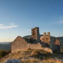 Ruines d'un château médiéval à Châteauneuf-les-Moustiers, baignées par la lumière dorée du soleil couchant, dominant un paysage de collines verdoyantes.