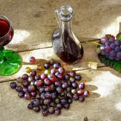 Nalewka z winogron na spirytusie w karafce, kieliszek z winem, winogrona i korek na drewnianym stole.