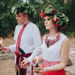 Para młoda w tradycyjnych strojach, z wiankami na głowach, trzymająca płonące świece. To piękna swadźba.