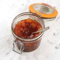 En burk med hemlagad mango chutney, perfekt för ditt nästa mango chutney recept. En sked vilar i den söta, kryddiga blandningen.