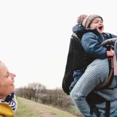 Szczęśliwa rodzina na spacerze. Tata niesie dziecko w nosidełku turystycznym, mama uśmiecha się do nich.