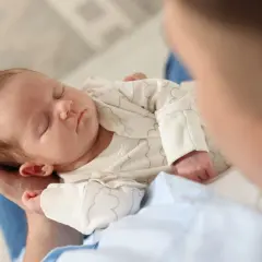 Un neonato dorme sereno tra le braccia di un genitore, cullato dal dolce rumore bianco che favorisce il sonno.