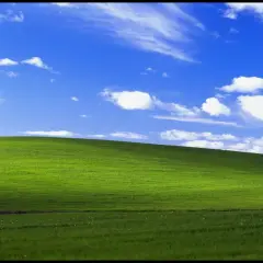 Zielone wzgórze pod błękitnym niebem z chmurami, ikoniczny widok z **win xp virtual machine**.