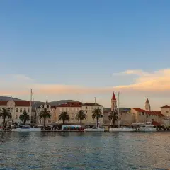 Trogir co zobaczyć: malownicza starówka z palmami i żaglówkami przy nabrzeżu, w blasku zachodzącego słońca.