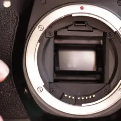 Zbliżenie na wnętrze lustrzanki EOS 60D. Palec wskazujący delikatnie dotyka jej obudowy, gotowy do uchwycenia chwili.