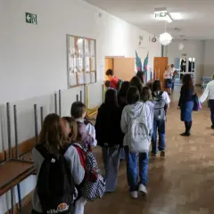 Uczniowie w kolejce na szkolnym korytarzu, w tle stoły do tenisa stołowego.