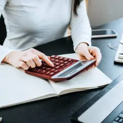 Kobieta liczy wydatki na własne cele mieszkaniowe, przygotowując PIT-39. Na biurku kalkulator, notatnik i laptop.