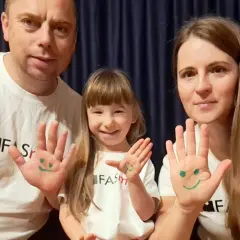 Uśmiechnięci dorośli z FAS i ich córka pokazują dłonie z namalowanymi buźkami.