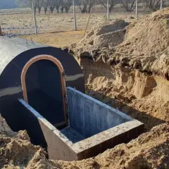 Budowa piwnicy ziemianki w trakcie. Okrągły, betonowy tunel z wejściem wkopany w ziemię, otoczony usypanym piaskiem.