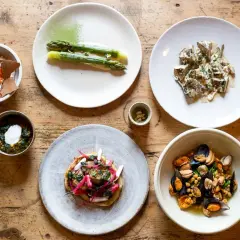 Assortiment de plats gastronomiques : asperges, moules, tartare, et autres mets fins sur table en bois.
