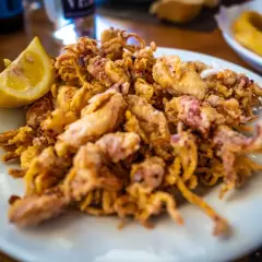 Un plato de puntillas de calamar fritas, doradas y crujientes, con un gajo de limón.