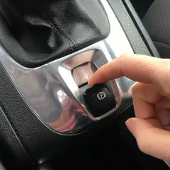 Dito, un dito preme il pulsante del freno a mano automatico, un gesto comune per parcheggiare in sicurezza.