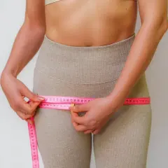 Mujer midiendo su cintura, observando la cinta métrica rosa que rodea sus caderas, enfocándose en los contornos y posibles hip dips.