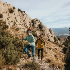 Deux randonneurs débutants progressent sur un sentier rocailleux, bâtons en main, sous un ciel bleu.
