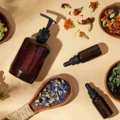 Botellas de vidrio ámbar con goteros y cucharas de madera con hierbas secas y flores, sugiriendo remedios naturales como flores de Bach para perros.