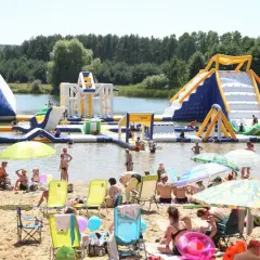 Ludzie bawią się na dmuchanych atrakcjach wodnych na **bolmin zalew**. Słoneczny dzień, plaża pełna wypoczywających.