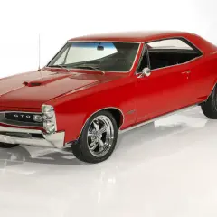 Klasyczny, czerwony Pontiac GTO z chromowanymi felgami, lśniącym lakierem i charakterystyczną atrapą chłodnicy.