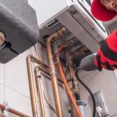Profesjonalny montaż pieca gazowego dwufunkcyjnego. Fachowiec w czerwonym ubraniu podłącza instalację.