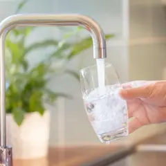 Un robinet verse de l'eau dans un verre, montrant comment obtenir de l'eau filtrée pour une boisson saine.
