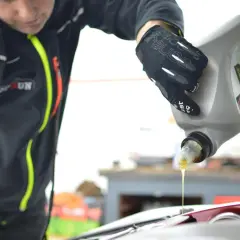 Mechanik w rękawiczkach nalewa olej do silnika. Dowiedz się, ile kosztuje wymiana oleju i filtrów u mechanika.