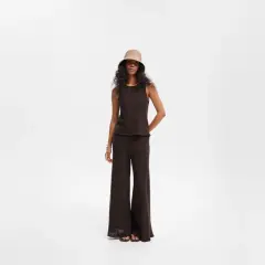 Modelka w brązowym topie i czarnych szerokich spodniach, uzupełniona kapeluszem typu bucket hat. Stylowe czarne szerokie spodnie stylizacje.
