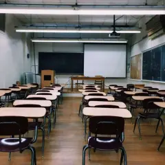 Pusta sala lekcyjna z rzędami ławek i krzeseł, tablicą i mapą świata.