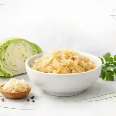 Parująca miska z kapustą kiszoną gotowaną, obok świeża kapusta, łyżka z kiszonką i słoik.